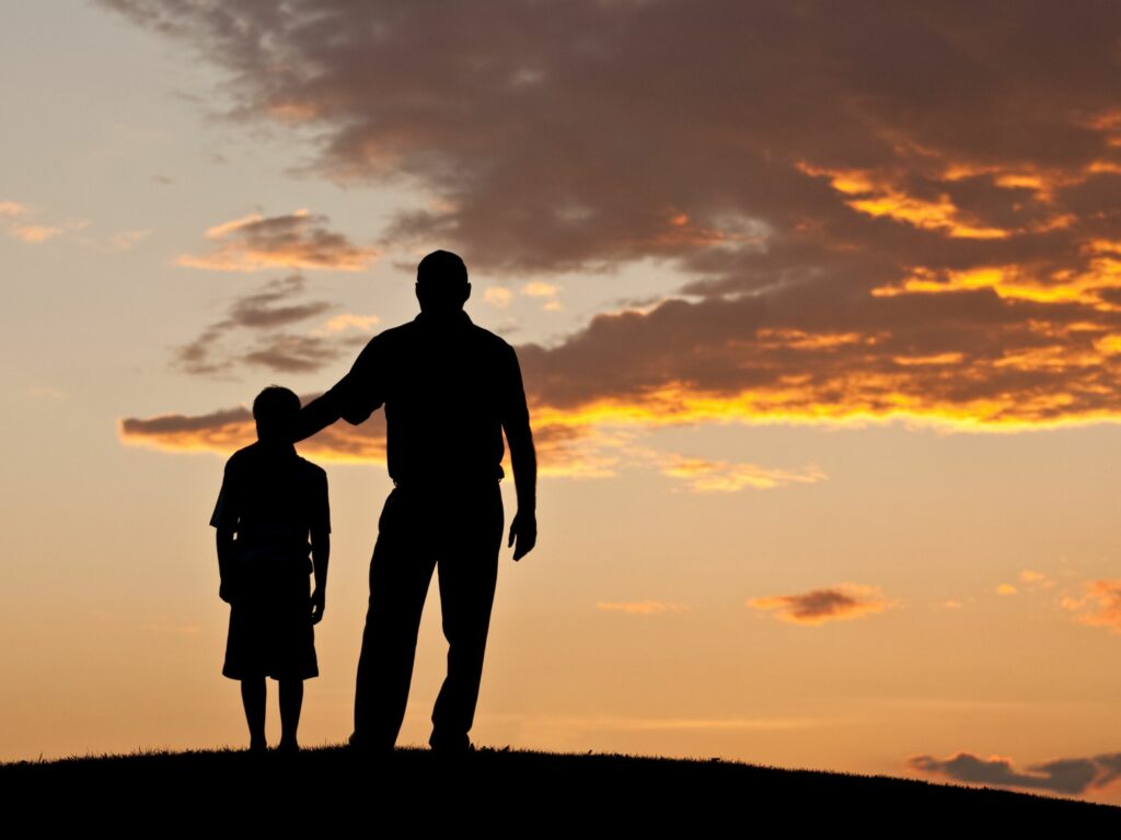 Father and son silhouette against sunset sky
